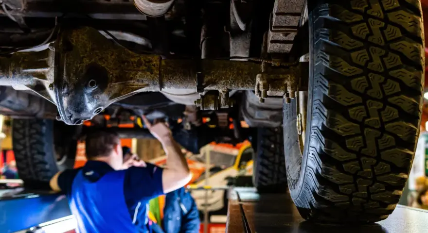 Mechanik bada podwozie terenowego Forda 4x4. Widoczna masywna oś i bieżnik opony.
