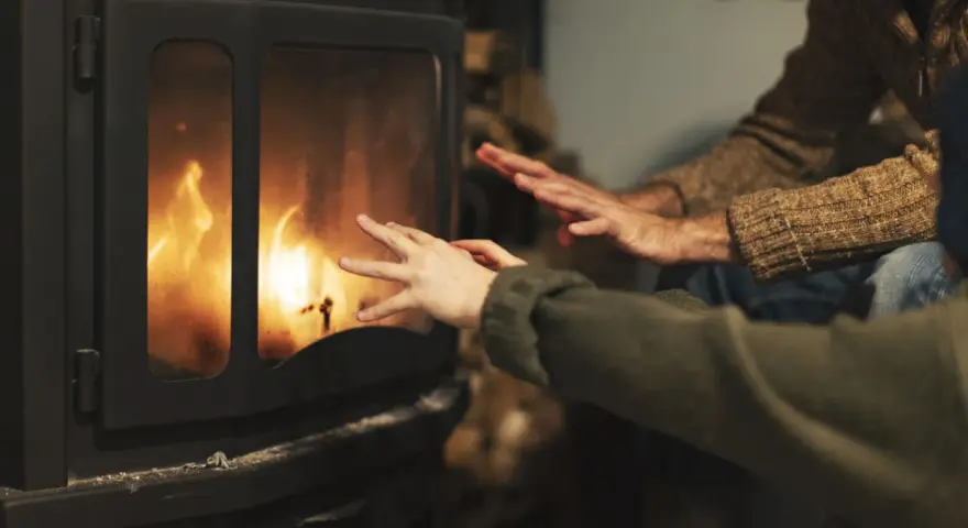 Manos calentándose frente a una chimenea con llamas danzantes. Los tubos de aire de la chimenea ayudan a distribuir el calor.