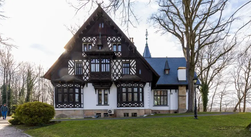 Pałac myśliwski w Promnicach, z charakterystyczną architekturą szachulcową i zdobieniami, otoczony drzewami.