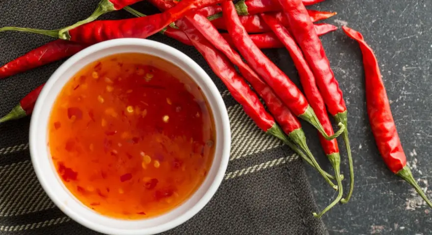 Frische rote Chilis neben einer Schüssel mit selbstgemachter Chili-Sauce. Perfekt zum Chili Sauce selber machen!