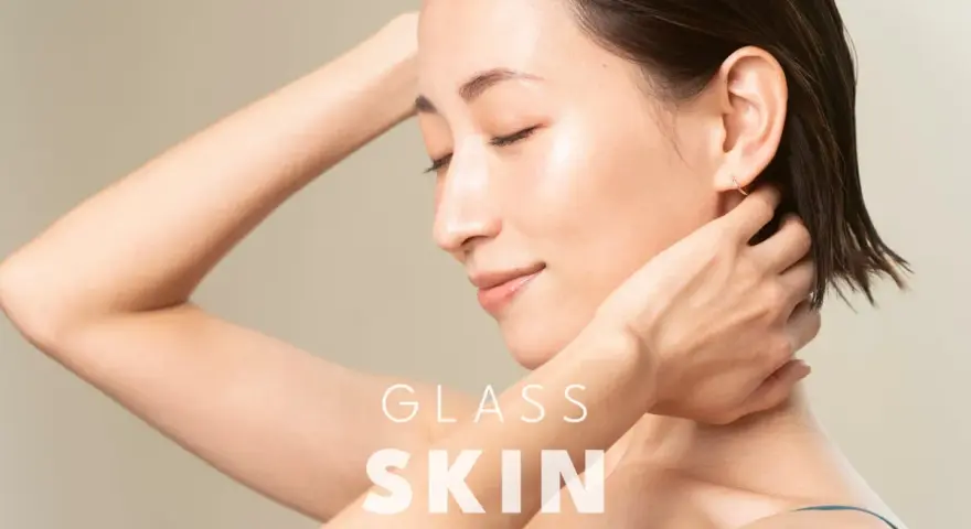 Kobieta z idealną, lśniącą cerą typu "glass skin", z dłońmi przy szyi i ramieniu.