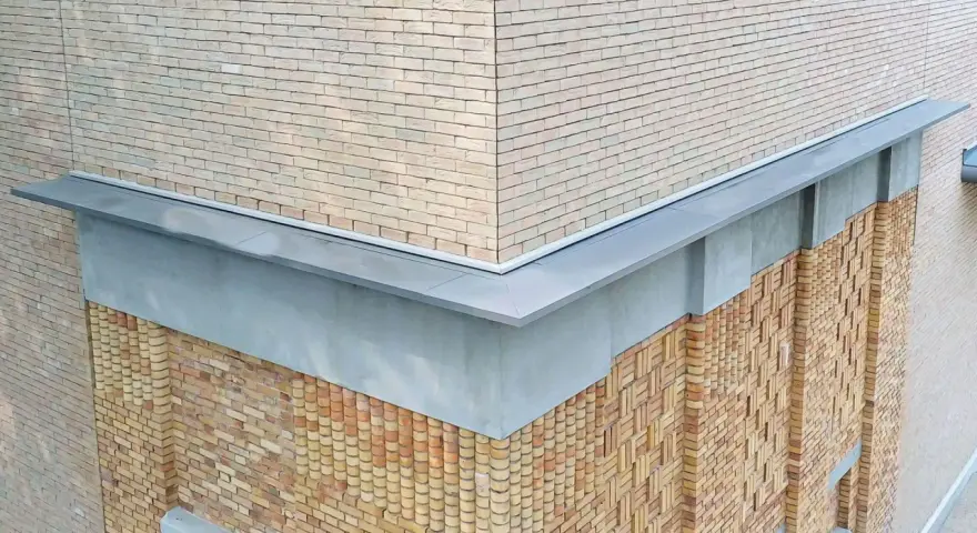 Narożnik budynku z ceglaną elewacją i nowoczesną attyką. Detale architektoniczne podkreślają fakturę muru.
