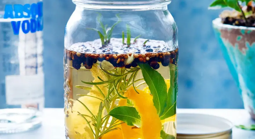 Ein Glas mit Zutaten für ein Sloe Gin Rezept: Wacholder, Zimt, Zitronenschale, Rosmarin und Lorbeerblätter in Alkohol.