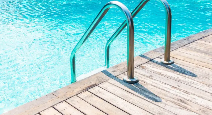 Escalera de piscina de obra con barandillas cromadas sobre tarima de madera. ¿Cuánto cuesta una piscina de obra?