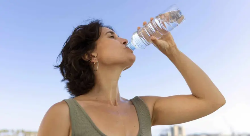 Donna beve acqua per combattere il caldo e la depressione, con il cielo azzurro sullo sfondo.
