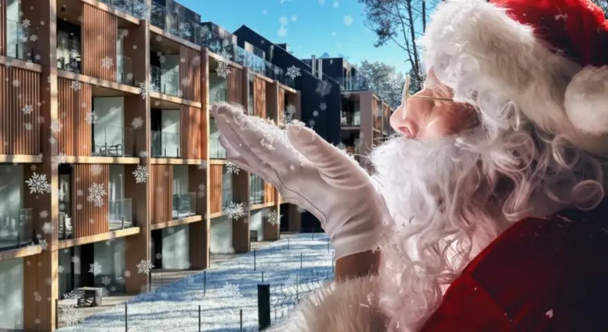 Śnieżynki tańczą wokół Świętego Mikołaja dmuchającego śniegiem na nowoczesny hotel. Czas na mikołajki w hotelu!