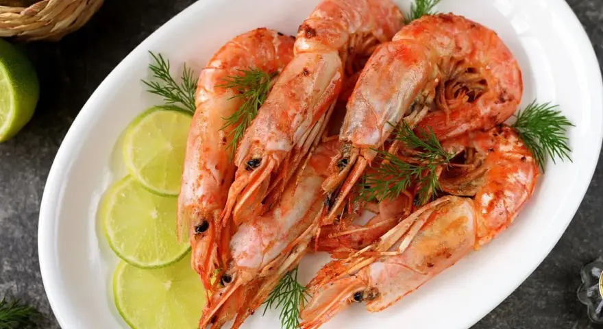 Plato blanco con langostinos cocidos, rodajas de limón y eneldo. Ideal para recetas con langostinos.