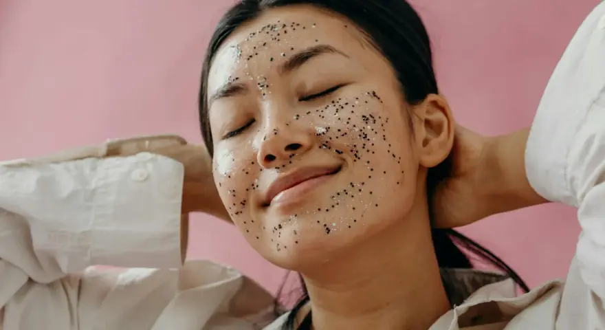 A woman with a sparkly exfoliating mask on her face, enjoying a moment of self-care. Over-exfoliation can sometimes lead to breakouts, so it's important to find the right balance.