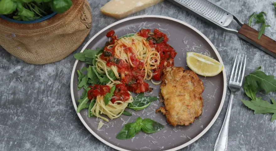 Piccata Milanese: goldbraunes Schnitzel mit Spaghetti in Tomatensauce, garniert mit Rucola und Zitrone.