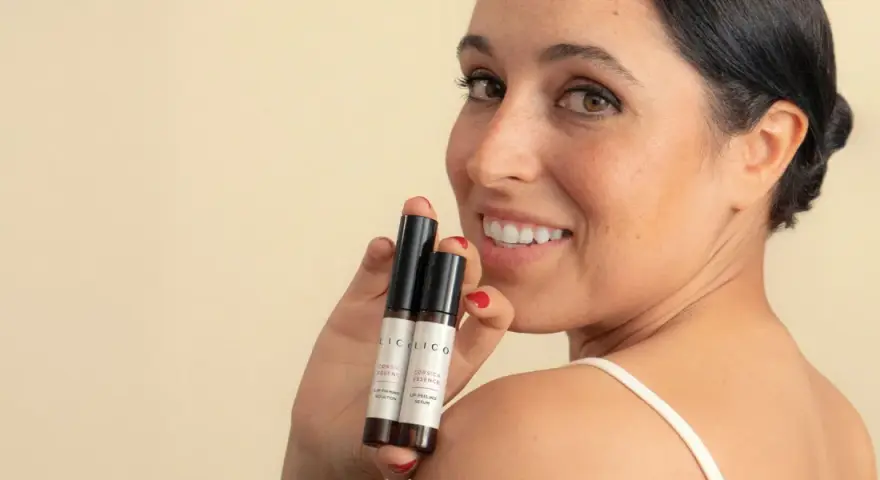 Mujer sonríe mostrando dos pequeños frascos, uno dice "Lip Peeling Serum", ideal para saber como exfoliar los labios.