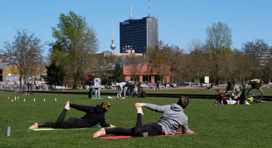 Menschen machen Yoga und entspannen sich im Park. Ein sonniger Tag für Sport in Berlin mit dem Fernsehturm im Hintergrund.