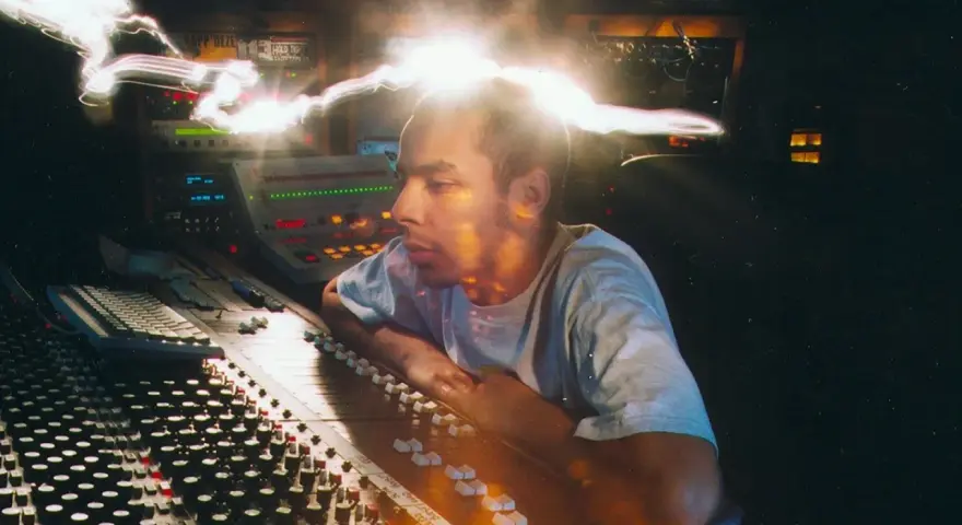 Un disc jockey célèbre, concentré, manipule une console de mixage dans un studio d'enregistrement, baigné de lumières vives.