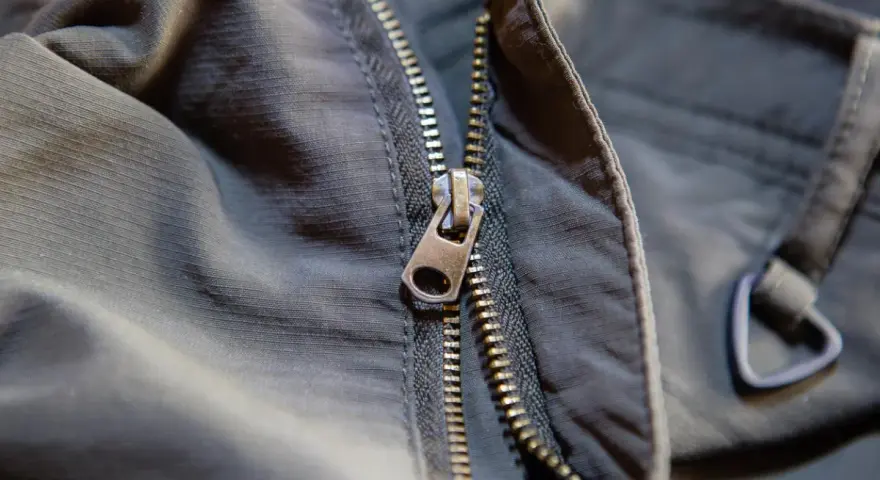 Detalle de una cremallera de chaqueta que se ha salido, mostrando el cursor metálico y los dientes.