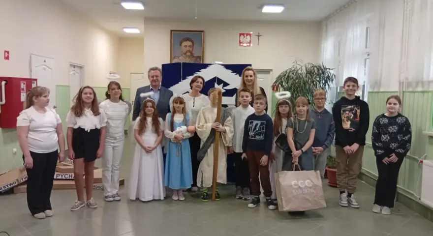 Dzieci w strojach aniołów i pasterzy, odgrywające baśń o dobrym synku. W tle portret i dekoracje.