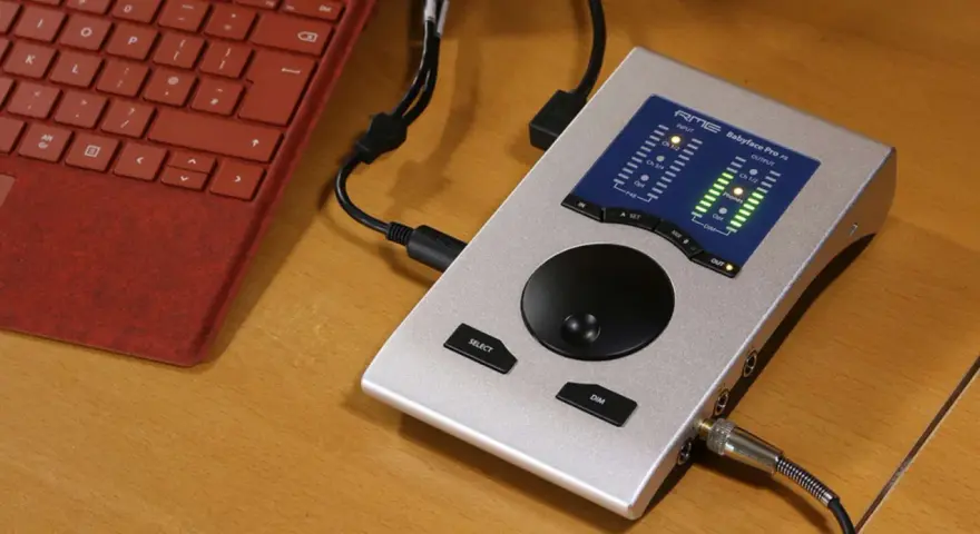 Srebrny interfejs audio RME Babyface Pro FS podłączony do czerwonej klawiatury. Idealny do mobilnego studia.