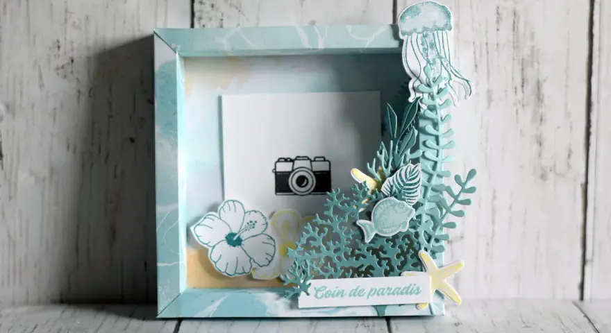 Un cadre photo en bois décoré sur le thème marin avec une méduse, des poissons, des fleurs et une petite caméra.