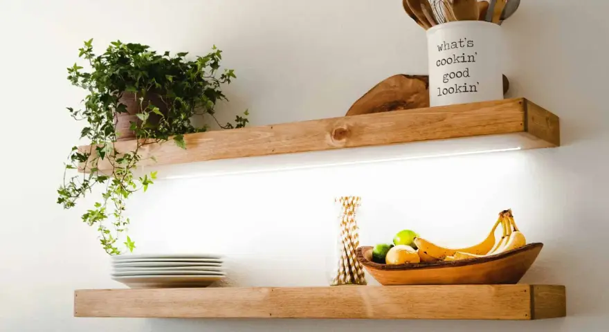 Estantes de madera con iluminación LED oculta, ideal para saber como colocar tiras led en estantes. Exhiben plantas, vajilla y frutas.