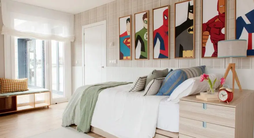 Habitación adolescente chico con cuadros de superhéroes, cama blanca con mantas verdes y cojines, mesita de noche de madera y ventana grande.