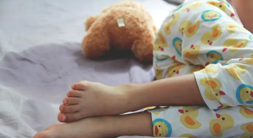 Ein Kind schläft im Pyjama mit Entenmuster, ein Teddybär liegt daneben. Es ist ein friedlicher Moment, in dem das Kind nachts ein und merkt es nicht.