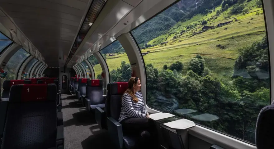 Kobieta w pociągu z panoramicznym widokiem na zielone szwajcarskie góry.