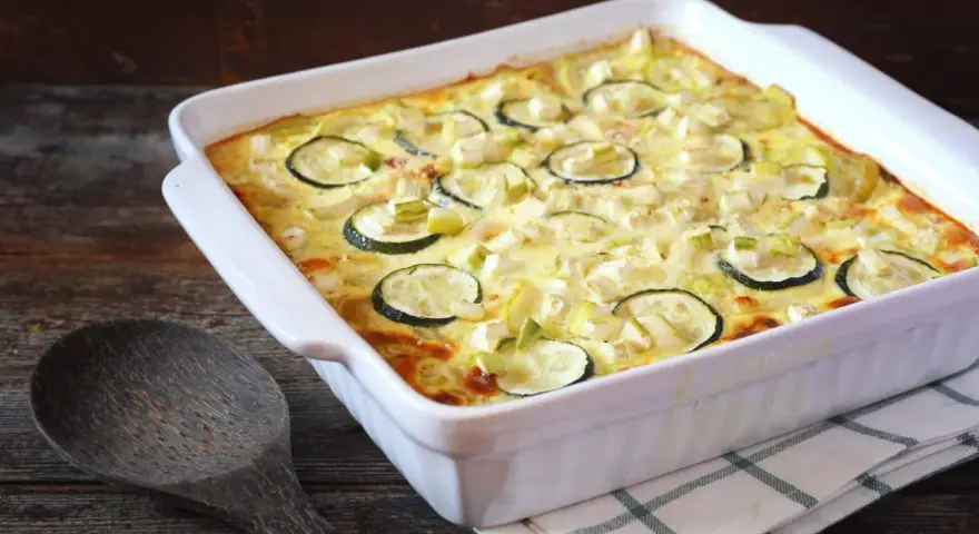 Un délicieux gratin de courgettes, prêt à être dégusté, avec des rondelles de courgettes et des morceaux de poireau dans une sauce crémeuse.