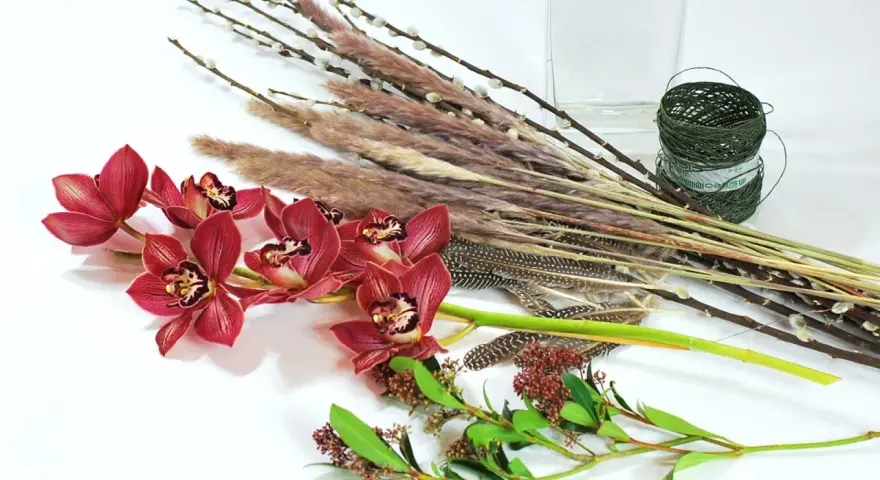 Ciemnoróżowe orchidee, trawy, pióra i gałązki tworzą kompozycję zrównoważoną.
