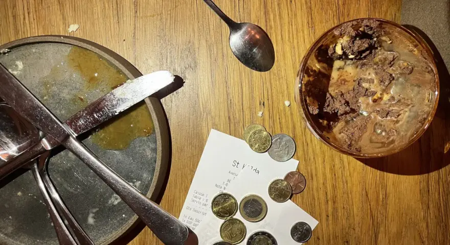 Sur une table en bois, un reçu et des pièces de monnaie sont posés près d'une assiette sale et d'un verre de dessert. Le patron peut-il garder les pourboires ?