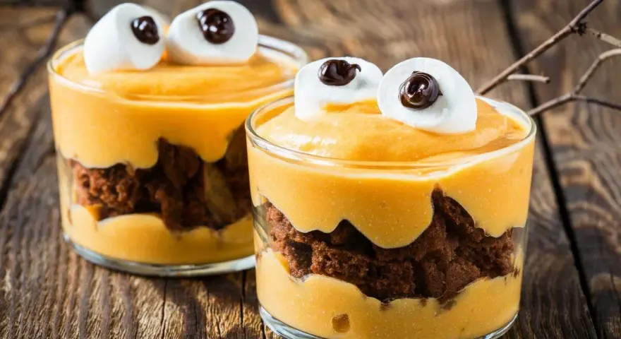 Przepis na Halloween: deser z mascarpone i ciastkiem czekoladowym, ozdobiony piankami jak oczy potwora.