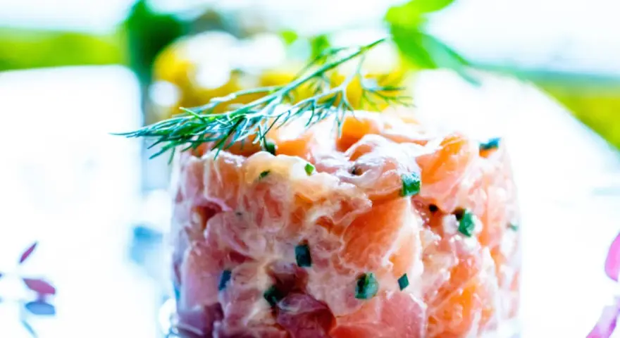 Tartare di salmone fresco, finemente tagliato e condito, guarnito con aneto. Un piatto leggero e saporito.
