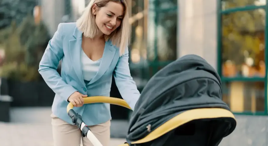 Uśmiechnięta kobieta w eleganckim stroju, z wózkiem dziecięcym, symbolizuje powrót do pracy po macierzyńskim.