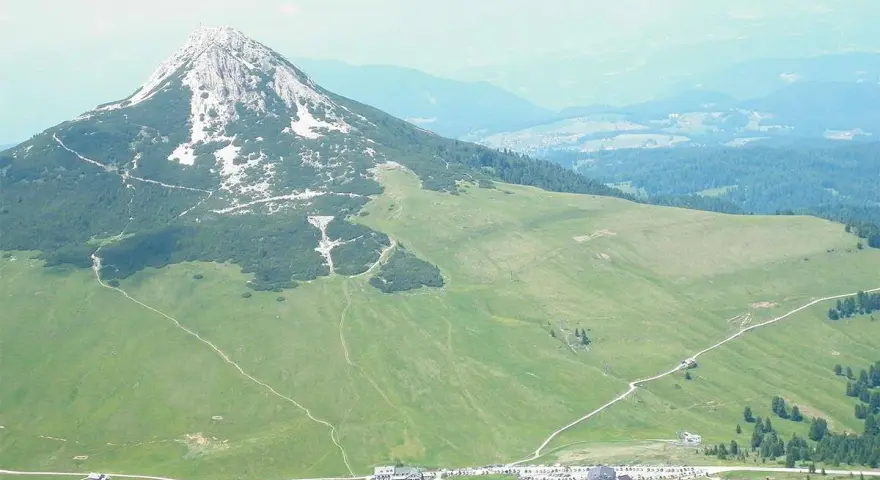 Panoramica delle malghe al Passo Lavazè, con un imponente monte sullo sfondo e sentieri che si snodano tra prati verdi.
