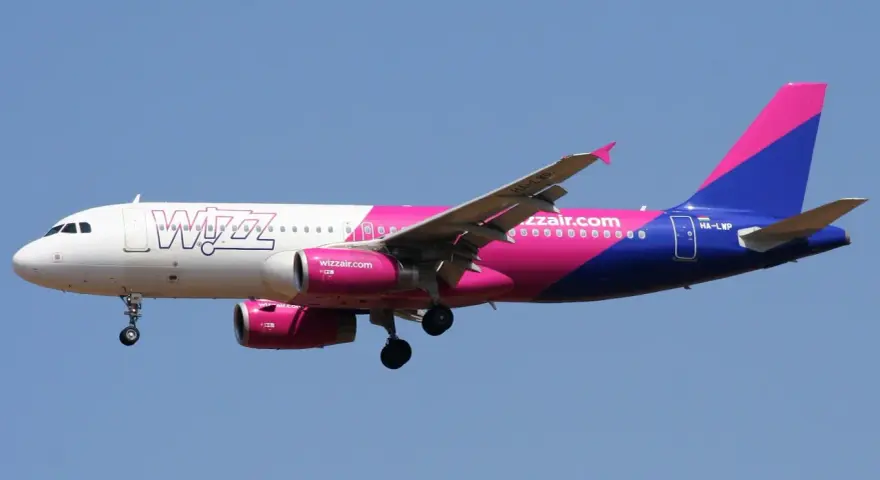 Samolot Wizz Air z różowo-fioletowym ogonem leci na tle błękitnego nieba. Sprawdź wizz discount club cena i leć taniej!