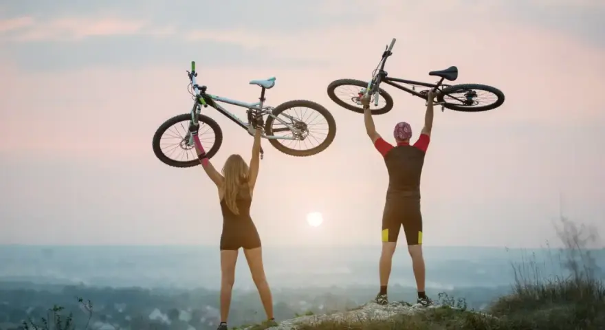 Para rowerzystów świętuje na szczycie, unosząc rowery. To idealny moment na odkrywanie najpiękniejsze odcinki z green velo.