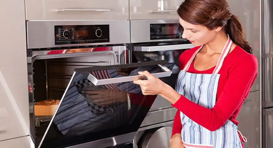Mujer con delantal abre horno donde se hornea un pan.