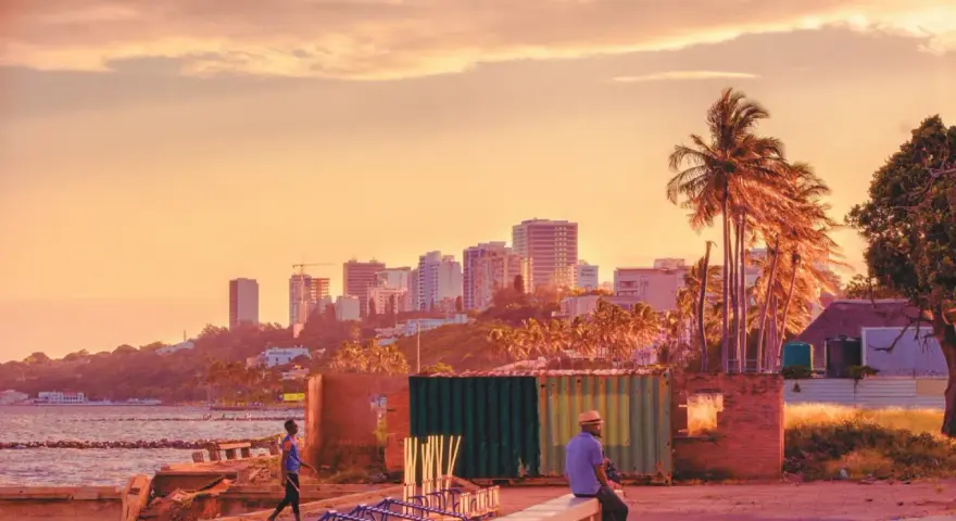 Zachód słońca nad Maputo, stolicą Mozambiku. W oddali widać panoramę miasta, a na pierwszym planie mężczyzna siedzi na murku.