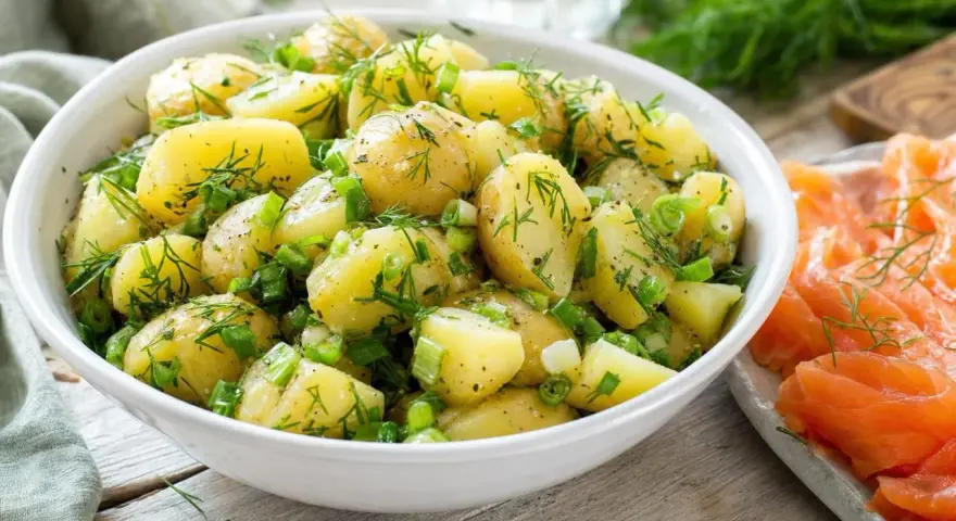 Salade de pommes de terre fraîchement préparée, garnie d'aneth et de ciboule, prête à être servie avec une sauce légère.