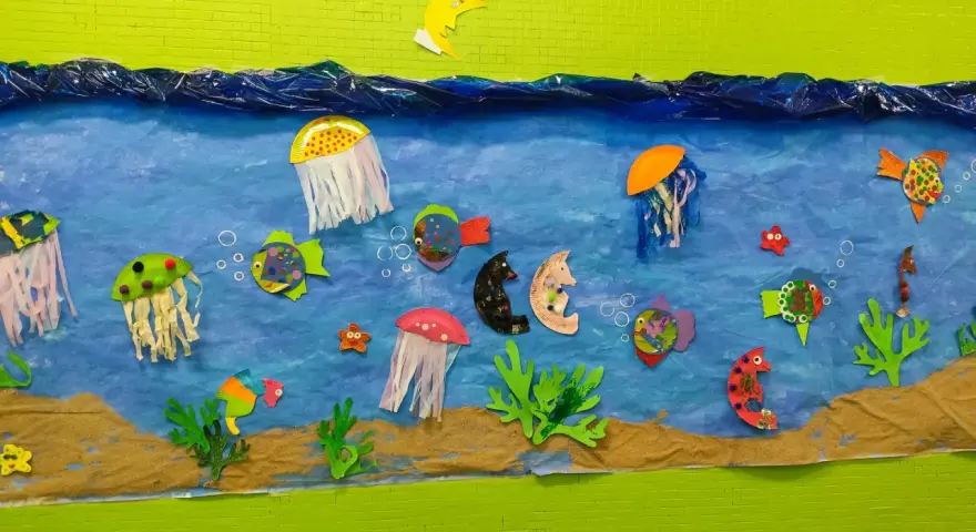Un colorido mural de animales marinos infantiles con peces, medusas y caballitos de mar nadando en un mar azul, sobre arena.