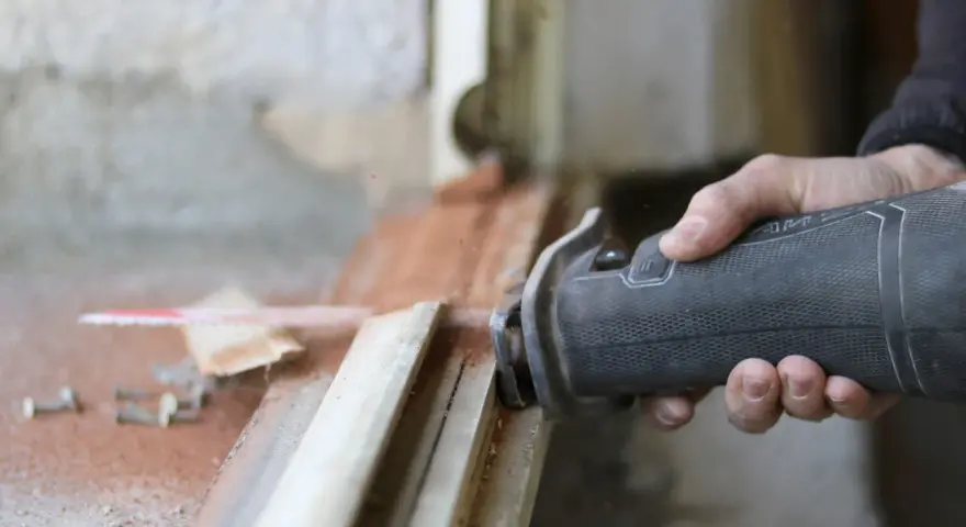 Main d'un artisan utilisant une scie sauteuse pour la dépose totale d'une fenêtre. Estimation du prix pose fenêtre dépose totale.