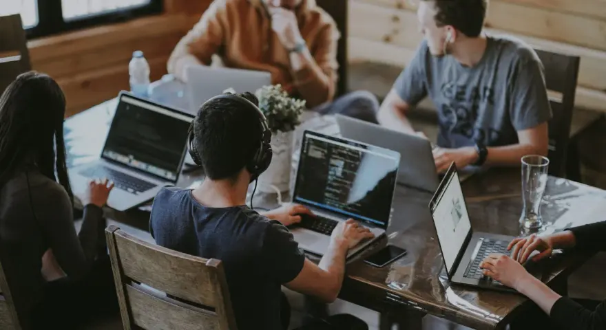 Un grupo de personas trabaja en sus portátiles en una mesa. Uno de ellos, con auriculares, parece concentrado en su pantalla, quizás buscando la clave del modelo 190.
