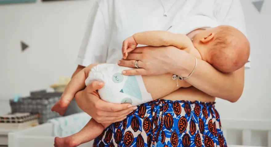 Mama tuli noworodka w pieluszce, idealnie jak ubierać noworodka latem. Lekkie ubranko i pieluszka to klucz do komfortu.