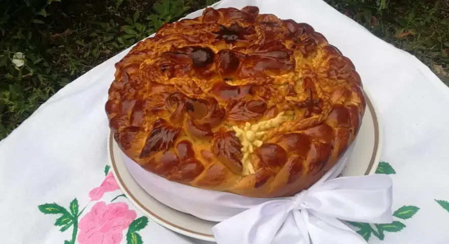 Obrzędowe ciasto weselne, bogato zdobione, z plecionkami i kwiatami z ciasta, na haftowanym obrusie.