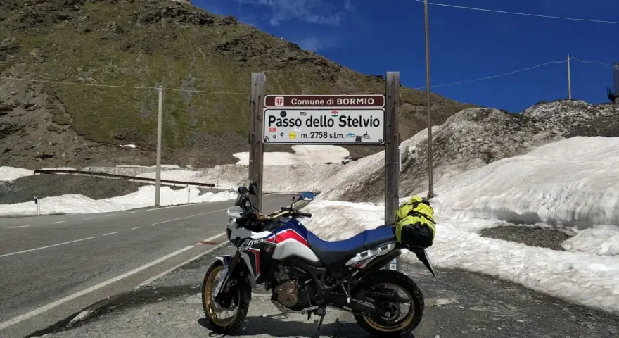 Moto pronta per affrontare il Passo dello Stelvio, con neve ai lati della strada e un edificio in cima alla montagna.