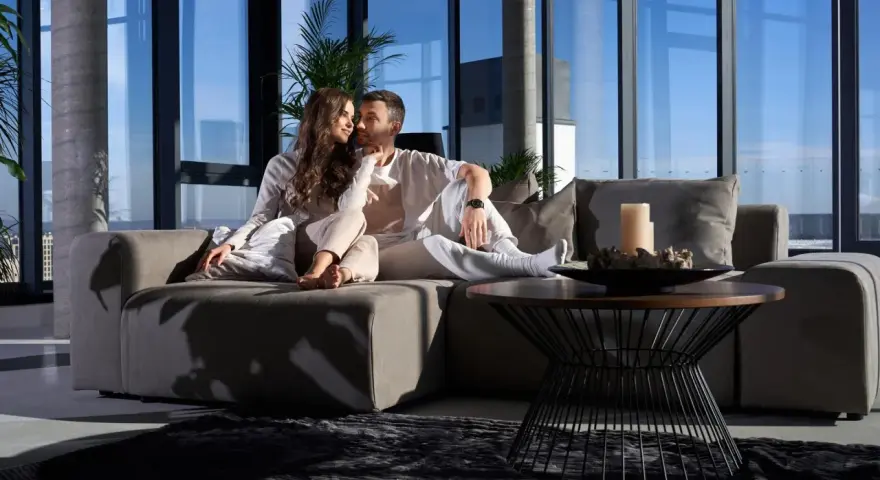 Pareja disfrutando de un momento íntimo en un sofá moderno, ideal para alquileres de temporada con vistas panorámicas.