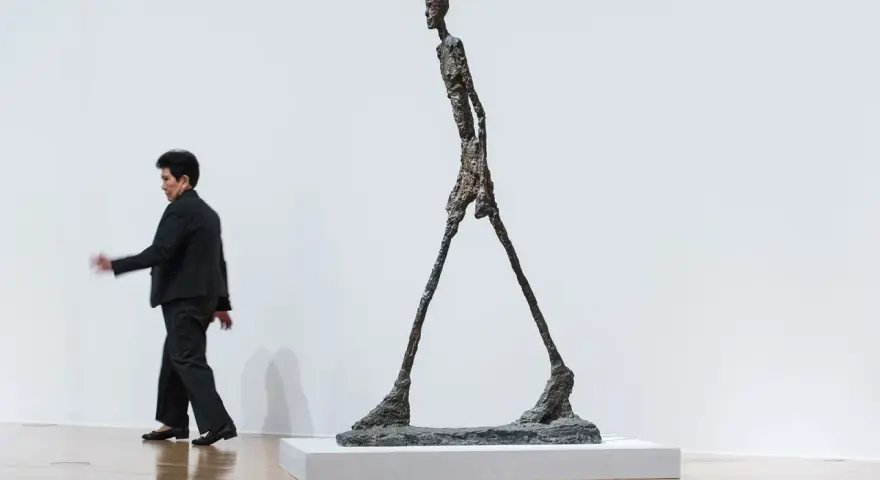 Un homme qui marche, une sculpture élancée, semble se déplacer dans un espace blanc.