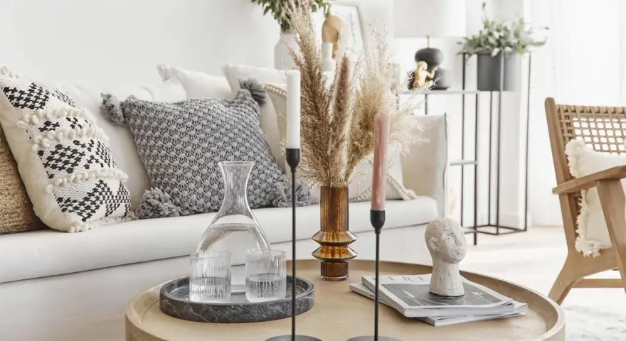 Tavolino rotondo in legno con elementi decorativi che evocano un'atmosfera boho chic: vasi, candele, libri e una scultura di testa.