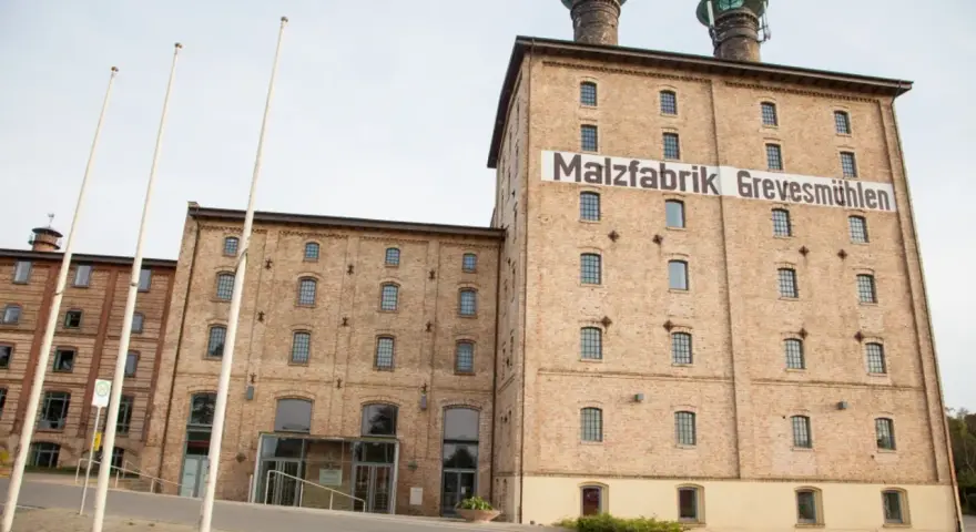 Die imposante Malzfabrik Grevesmühlen, ein Backsteingebäude mit markanten Türmen, steht im hellen Tageslicht.