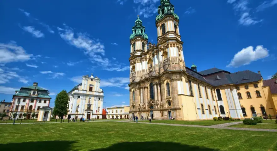 Barokowy kościół i klasztor na tle błękitnego nieba z chmurami. Piękne sanktuaria maryjne w Polsce zachwycają architekturą.
