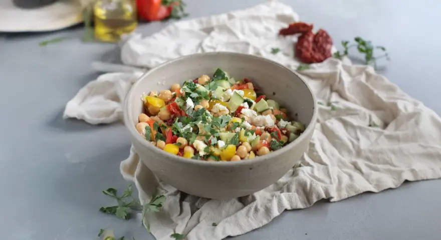 Ein bunter Kichererbsen Salat mit Gurken, Tomaten, Paprika und Feta, garniert mit frischer Petersilie.