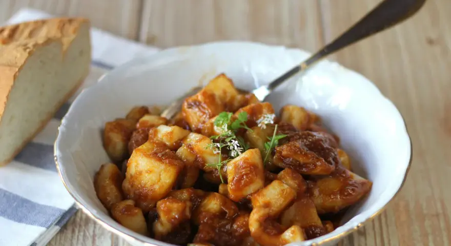 Un plato de sepia con patatas en salsa, decorado con hierbas frescas. Acompañado de pan rústico.