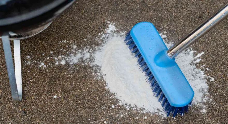 A blue brush is used to scrub a pile of white powder on a concrete patio, demonstrating how to clean concrete patio.